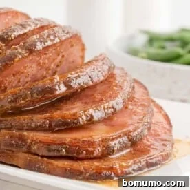 Perfectly sliced Crockpot ham with a glossy maple dijon sauce on a platter.