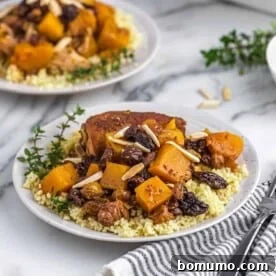 Two plates of Slow Cooker Moroccan Chicken Thighs with couscous and roasted squash, garnished with almonds.