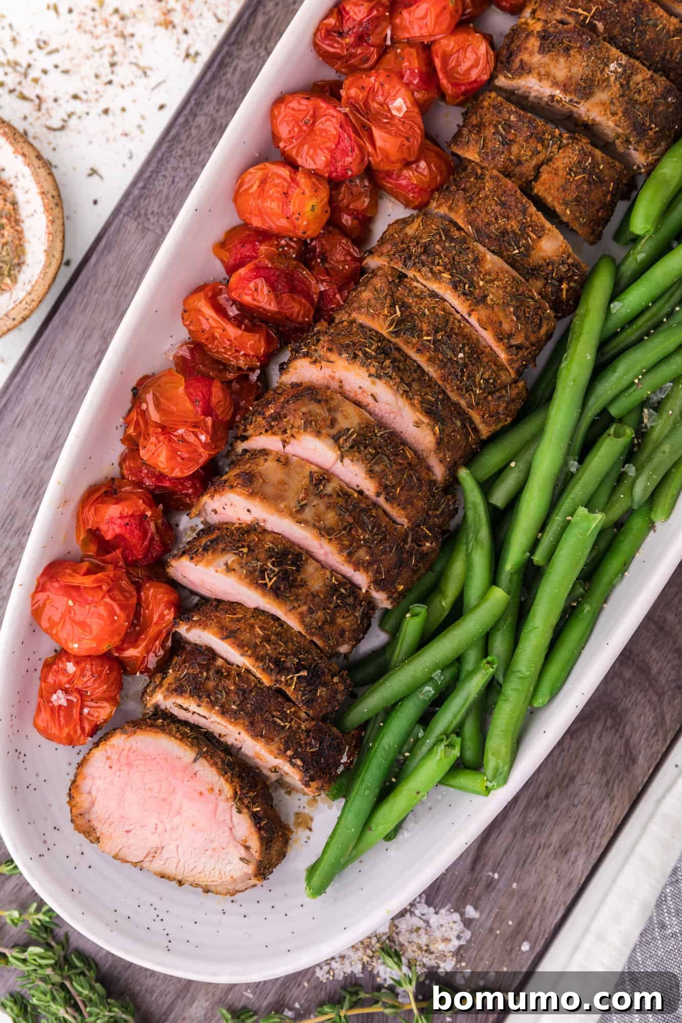 Pork tenderloin on platter with vibrant tomatoes and fresh green beans.