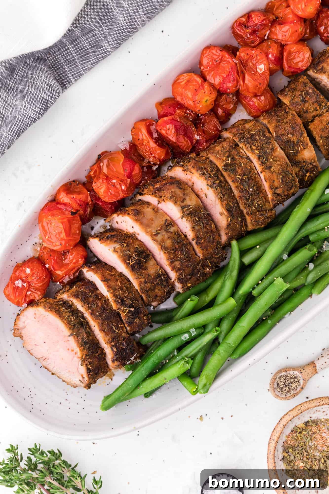 Pork on a platter with fresh green beans and colorful tomatoes.