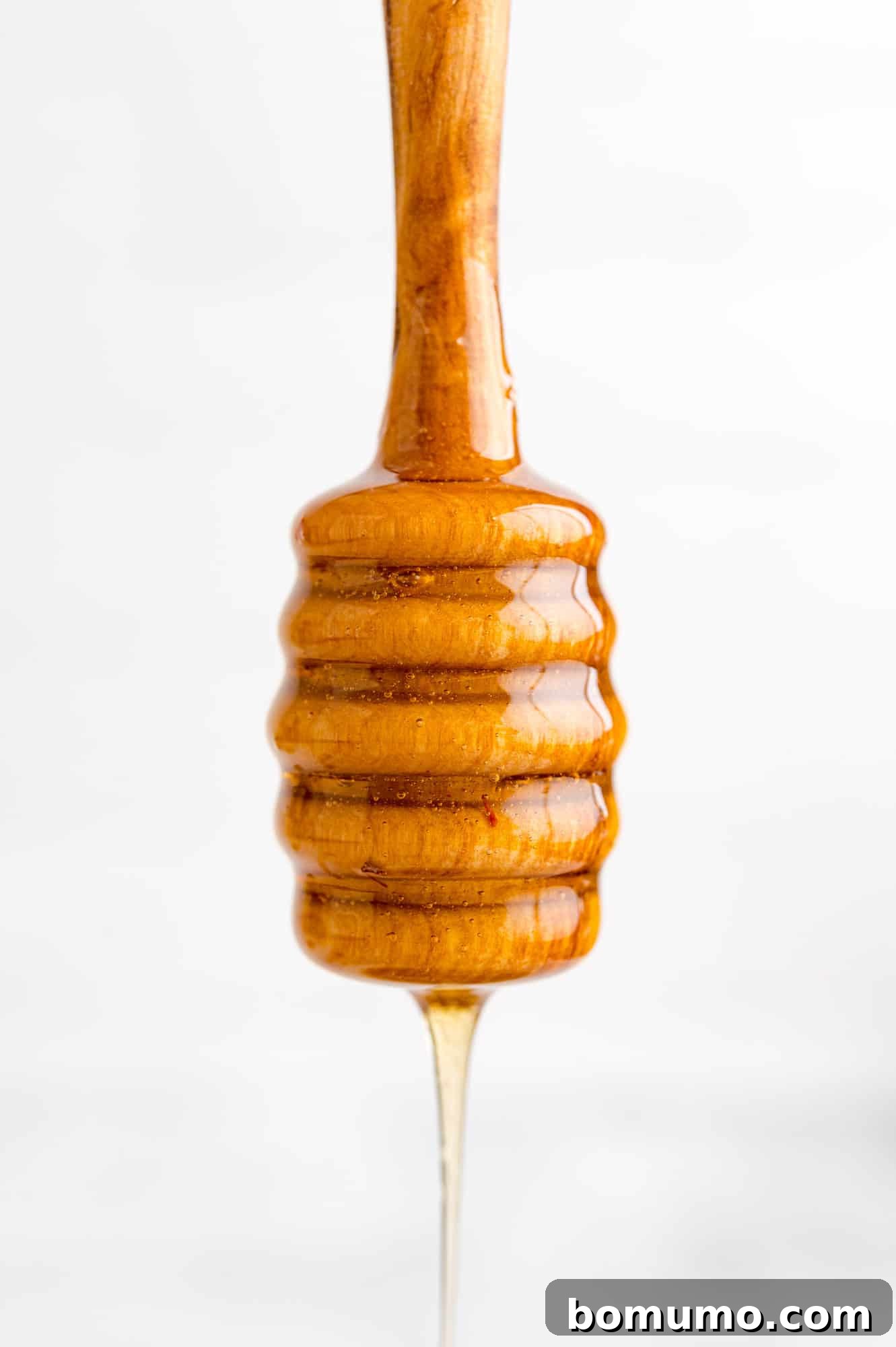 Golden honey dripping off a honey dipper, illustrating its luscious texture.