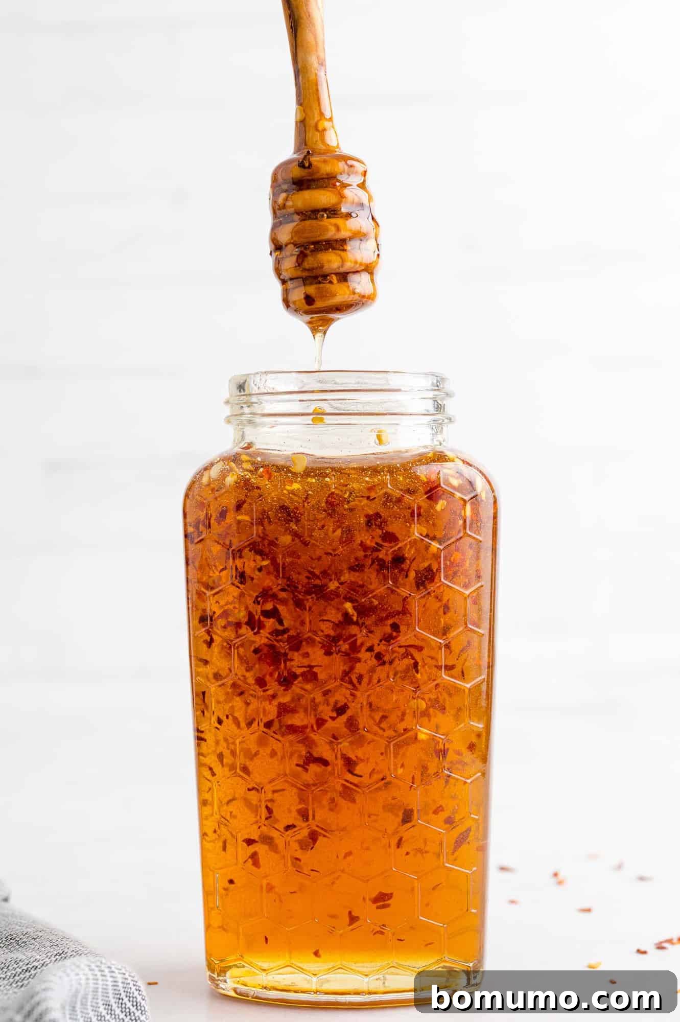 Hot honey in a jar with a honey dipper being lifted out, showcasing its sticky texture.
