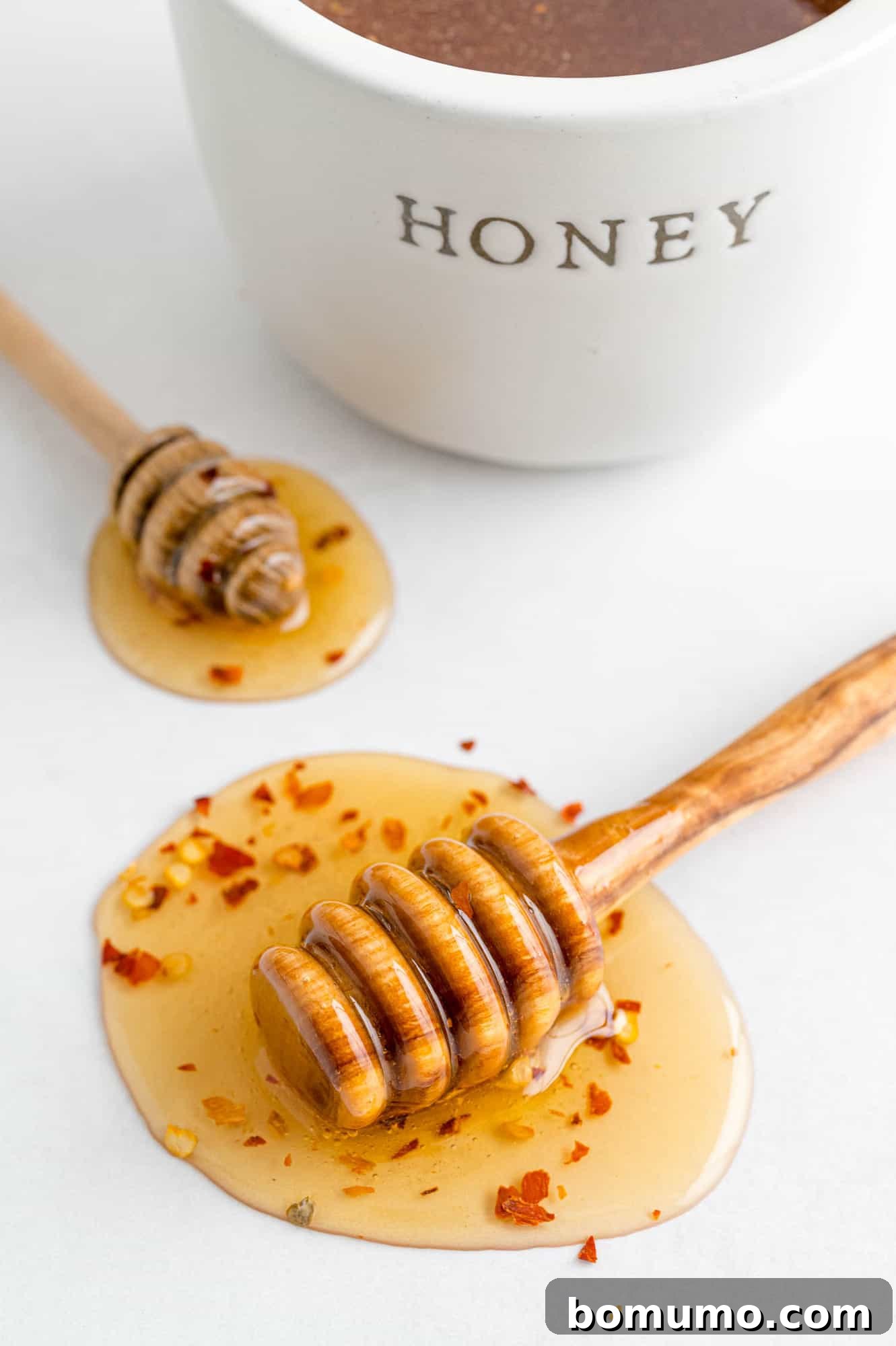 Hot honey with visible red pepper flakes on a clean white surface, highlighting its texture and color.