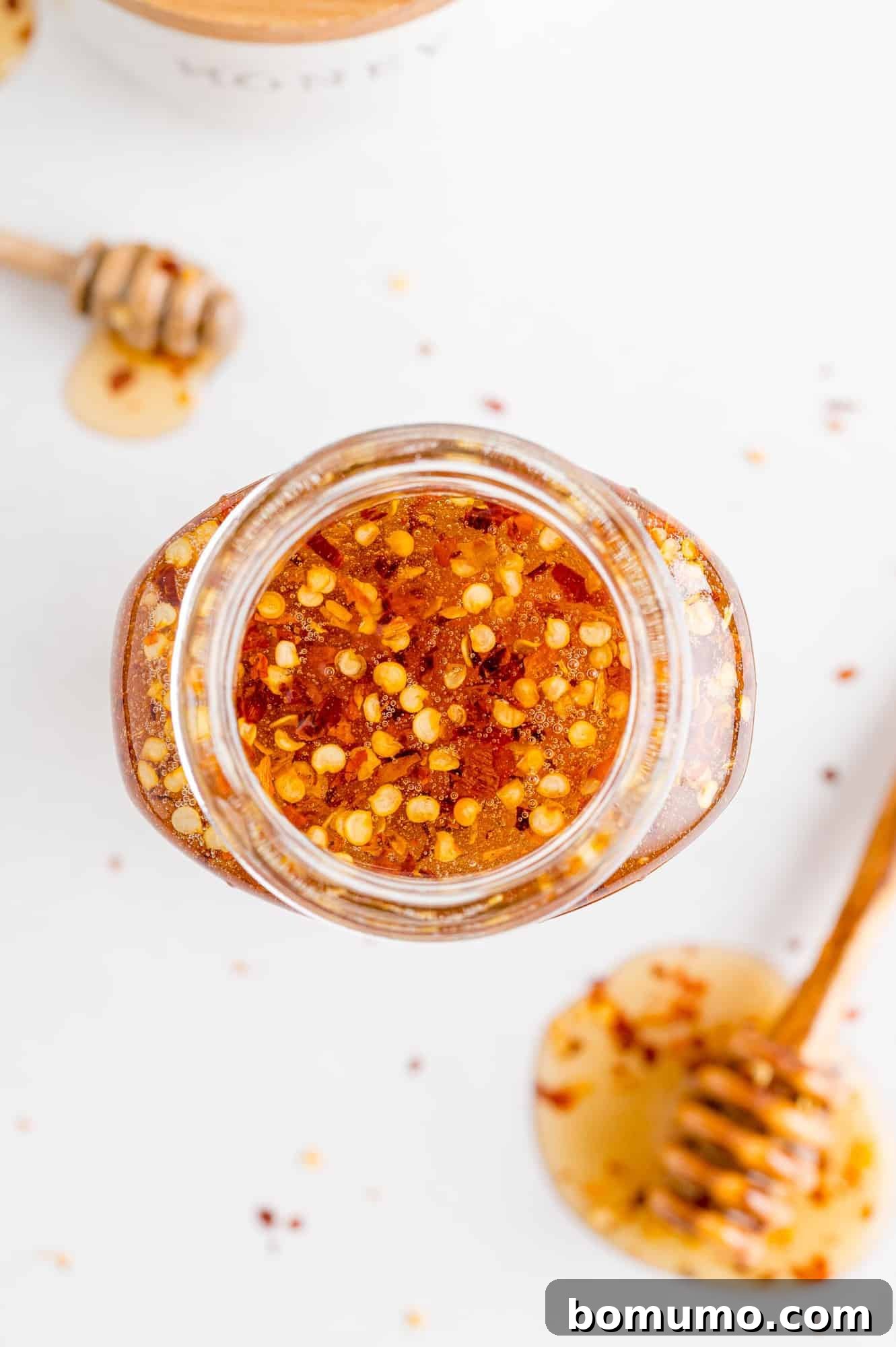 Overhead view of hot honey in a decorative jar and on a dipper, placed on a white surface.