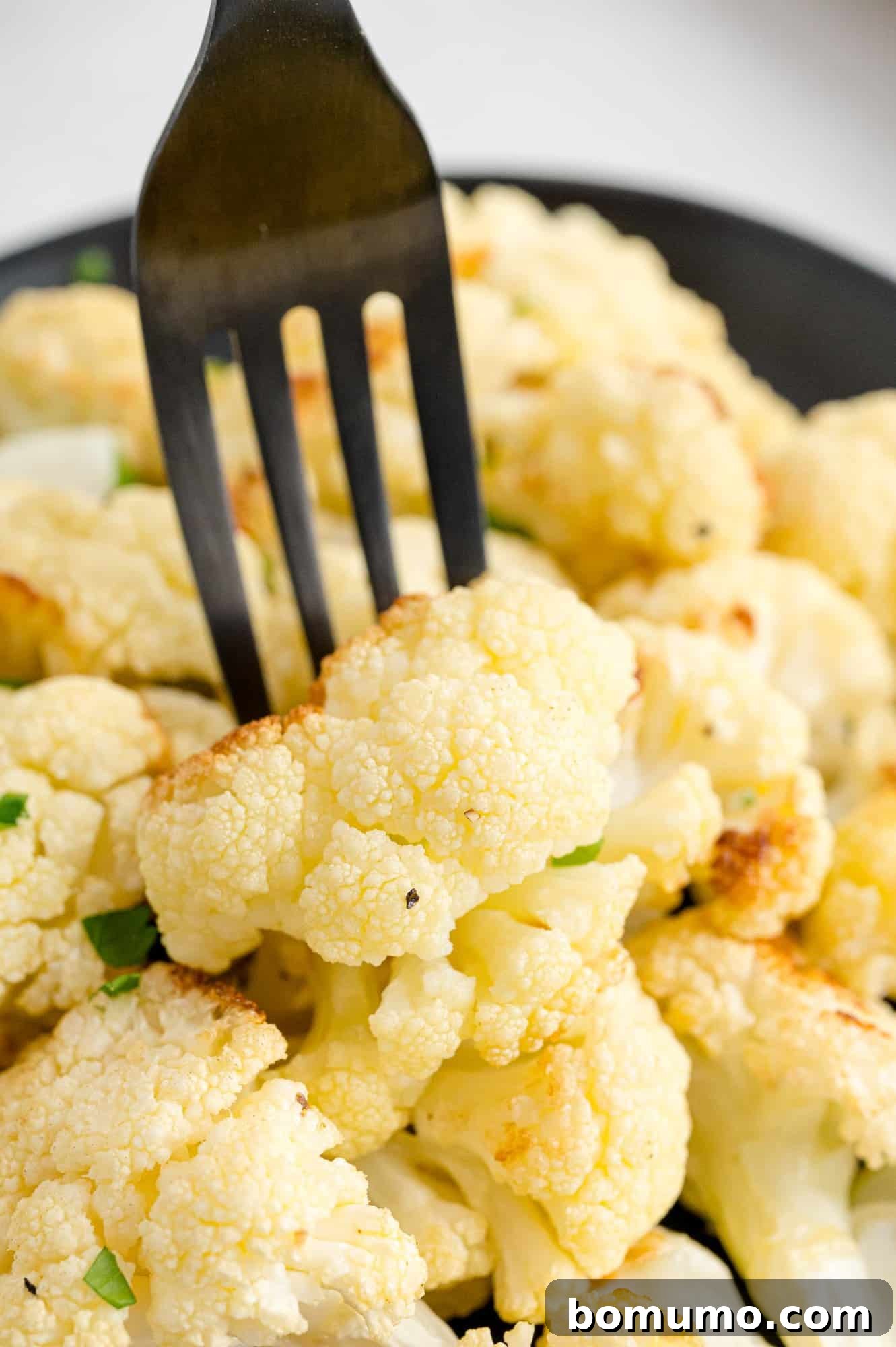 Perfectly Crispy Roasted Cauliflower 13 A piece of roasted cauliflower held on a black fork, showing its golden-brown texture.
