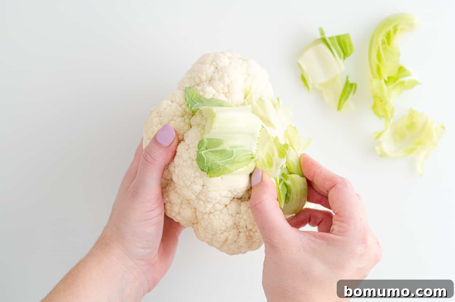 Perfectly Crispy Roasted Cauliflower 4 Leaves being removed from a head of cauliflower with a knife.