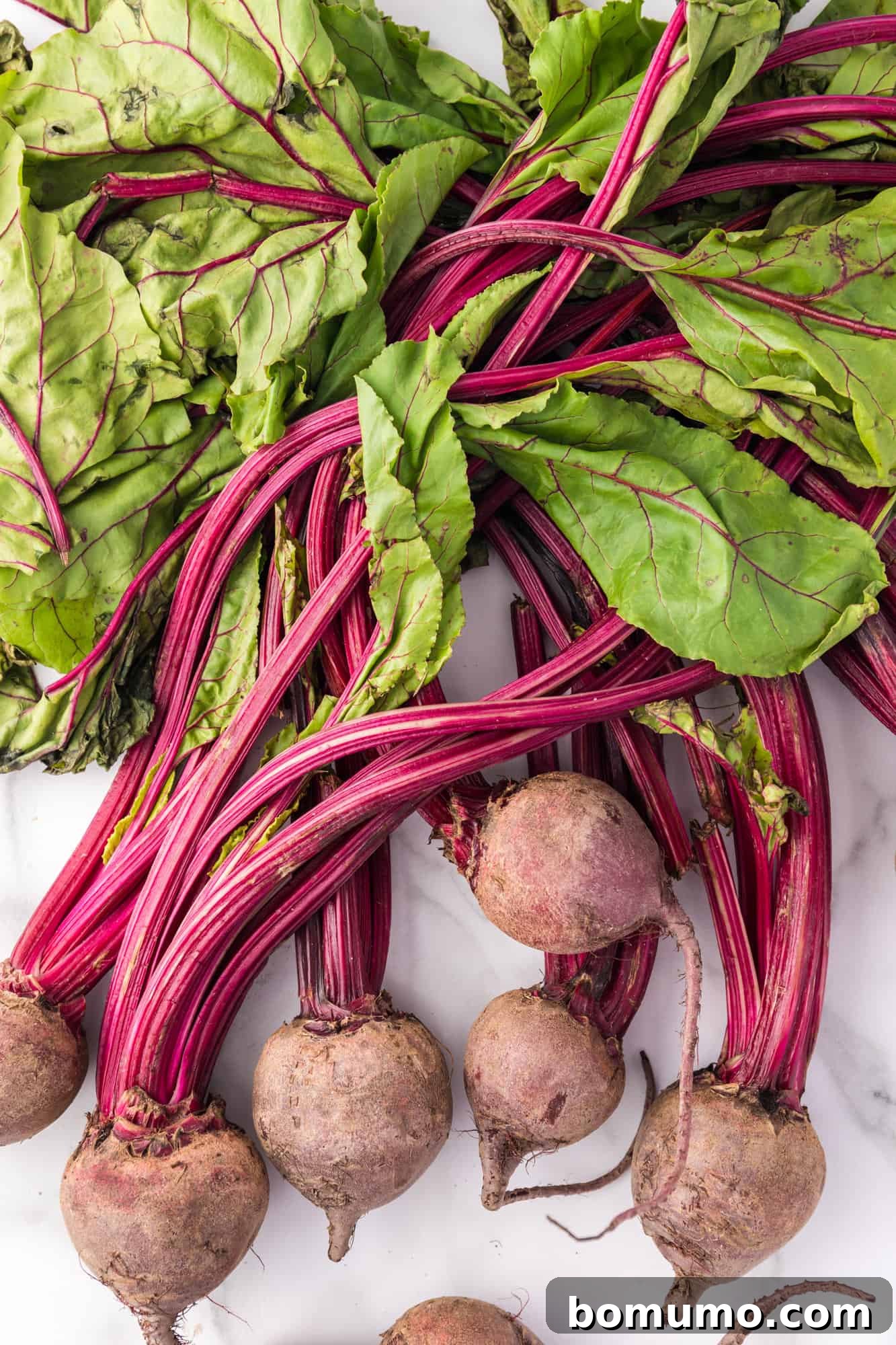 Freshly harvested beets with their green leaves still attached, lying on a wooden surface, highlighting their natural appeal.