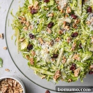 Brussels sprouts salad in a round clear glass bowl, on white marble background.
