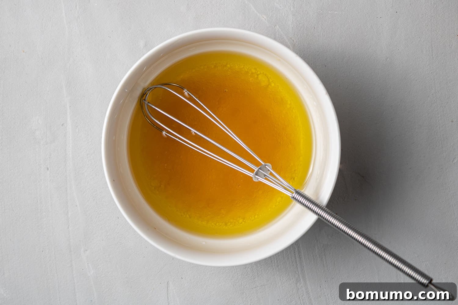 Homemade maple vinaigrette dressing in a small white bowl with a miniature whisk, ready to be added to the salad.