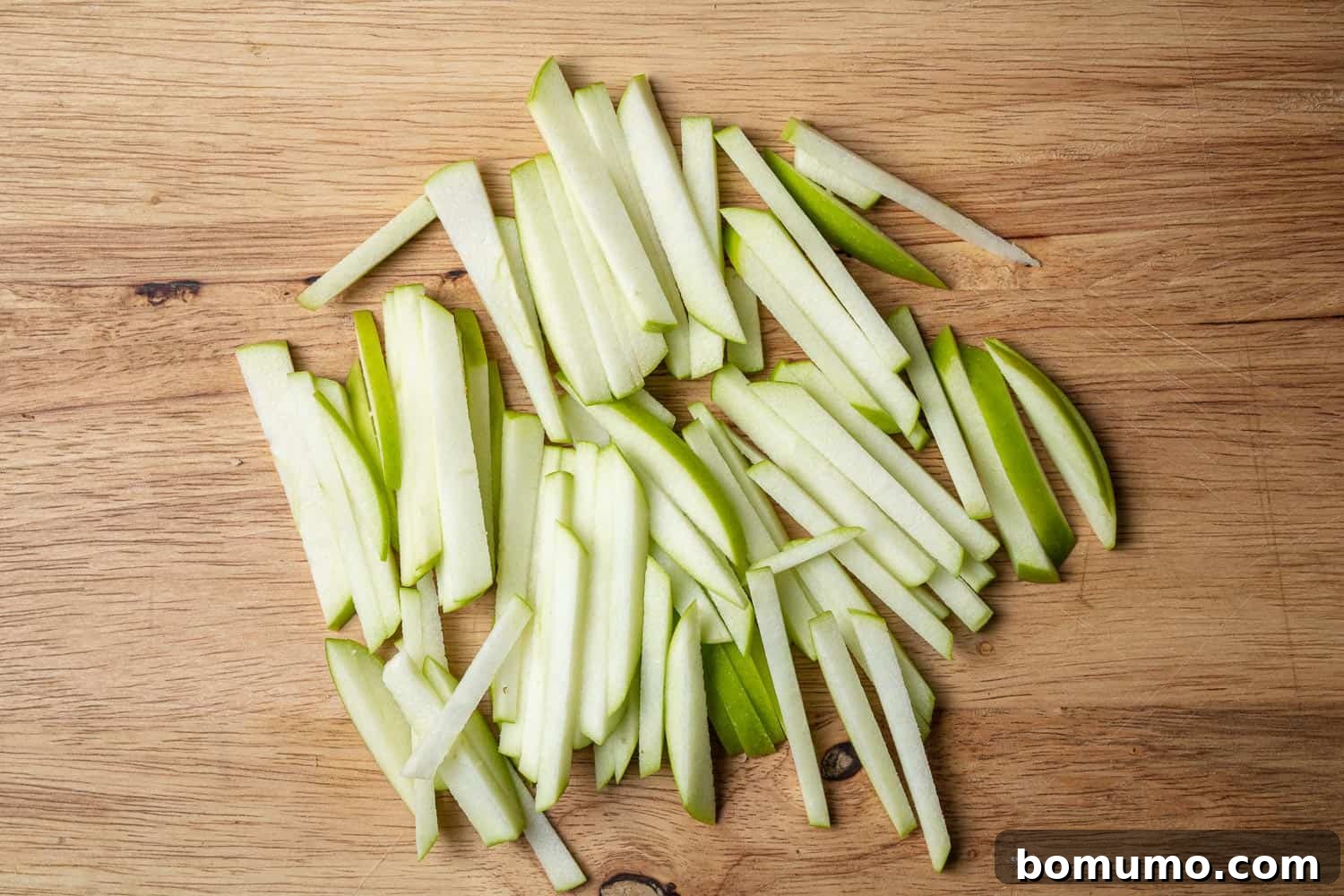 Freshly sliced green apples cut into matchsticks, arranged on a rustic wooden cutting board.