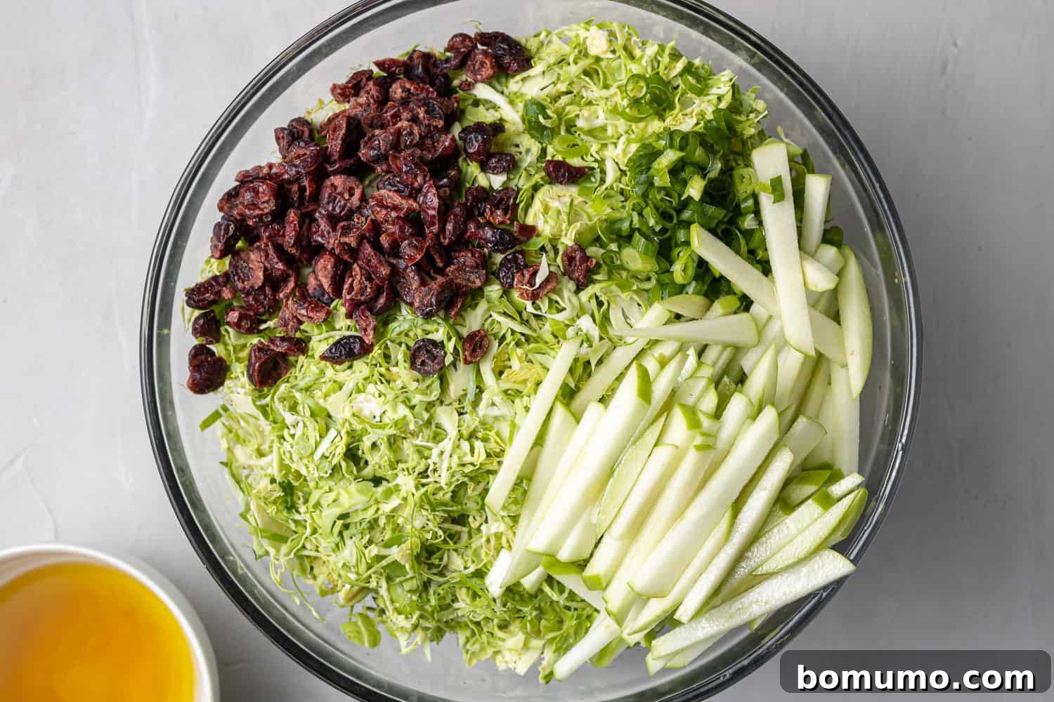 Unmixed Brussels sprouts salad with visible apples and cranberries, awaiting a final toss with the dressing.