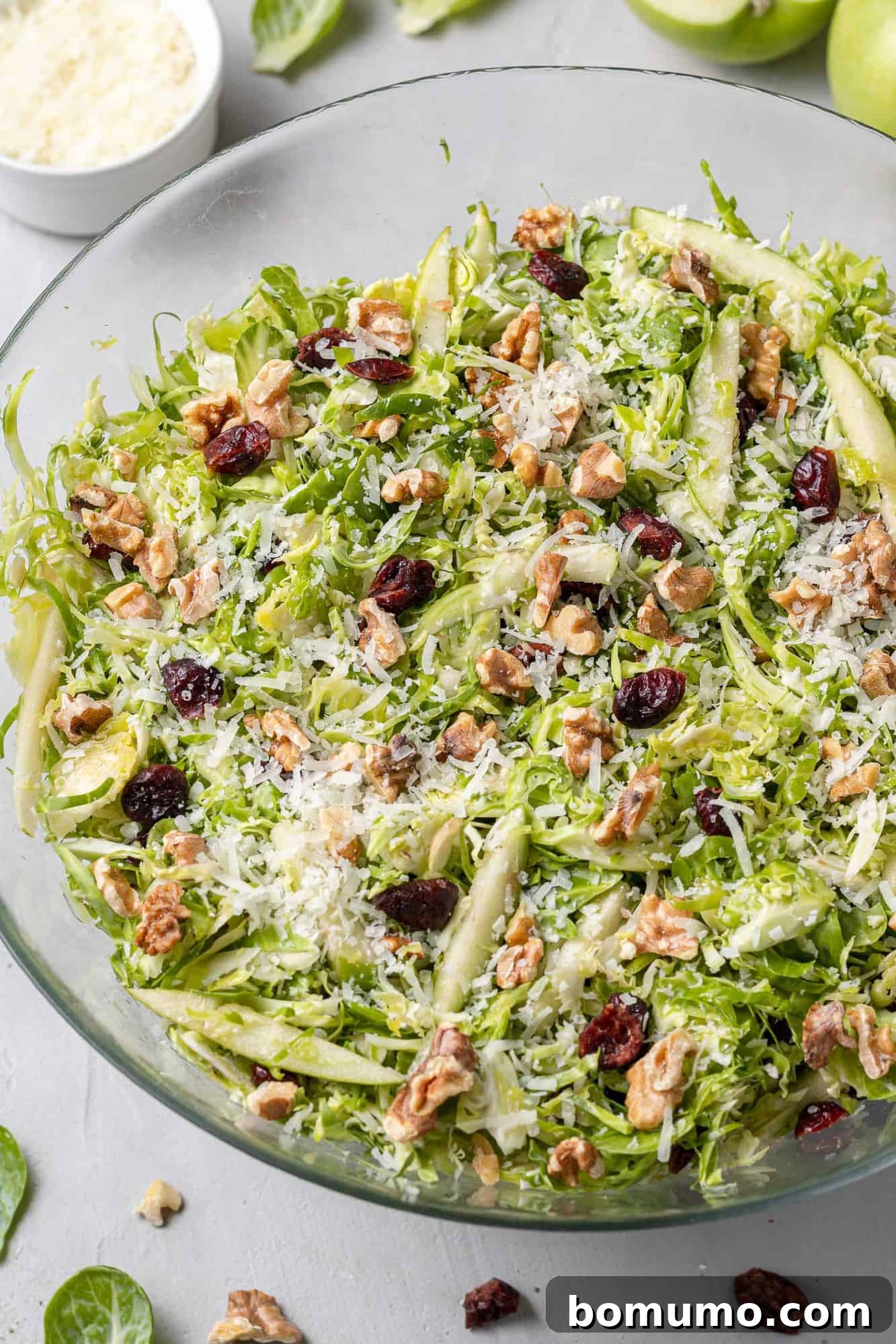Close up of a vibrant green Brussels sprout salad in a clear glass mixing bowl, showcasing the shredded texture.