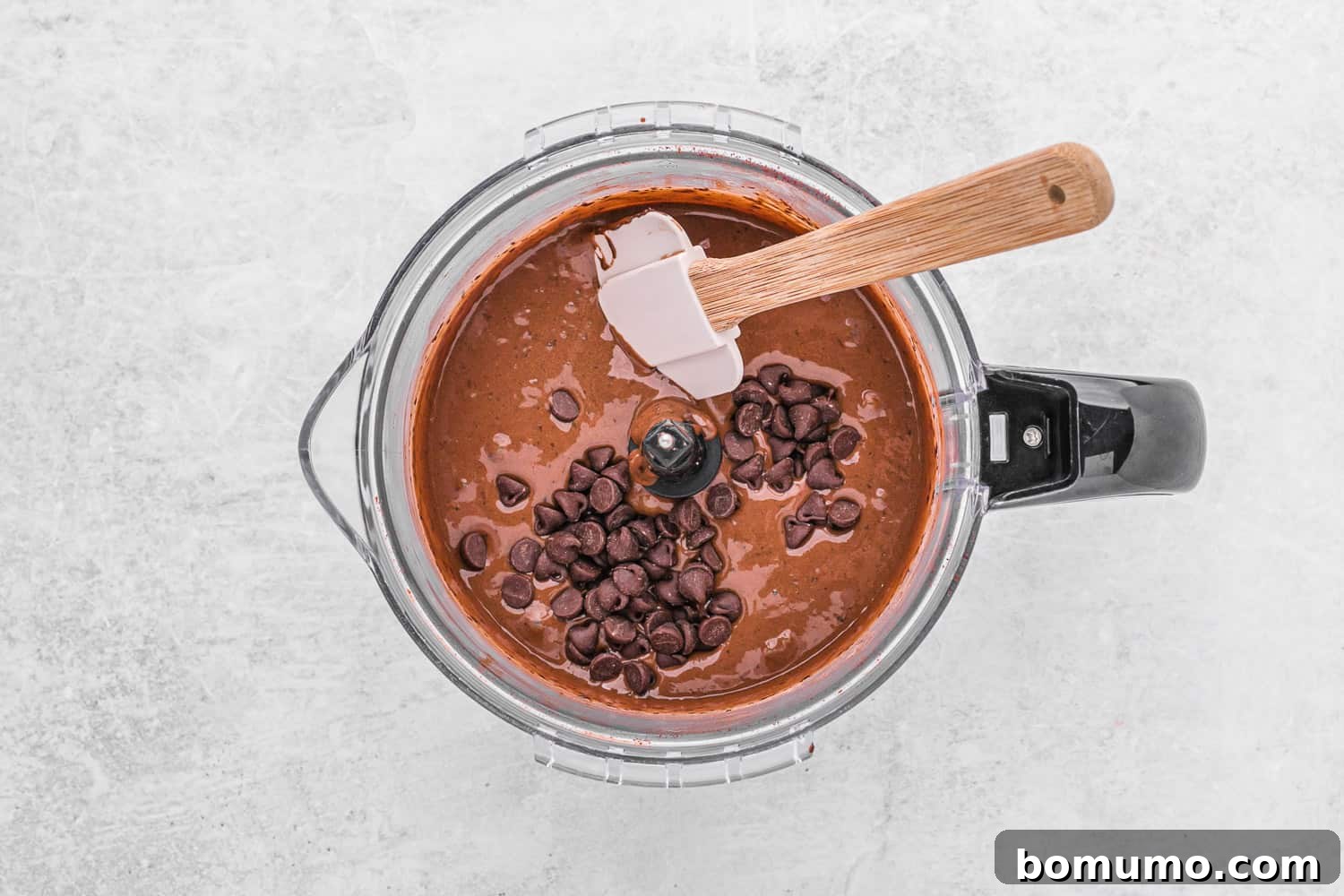 Semisweet chocolate chips being folded into black bean brownie batter with a spatula.