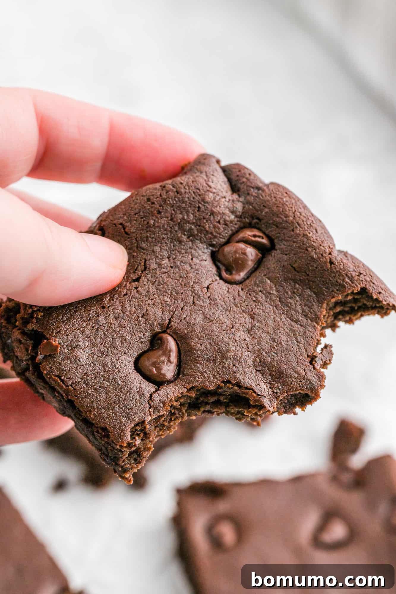 A hand holding a single fudgy black bean brownie.
