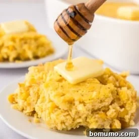 A portion of fluffy corn spoon bread, topped with butter and a drizzle of honey, served on a plate.