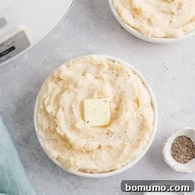 Fluffy crockpot mashed potatoes in a white serving bowl, garnished with fresh herbs.