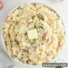 Buttery mashed red potatoes, garnished with fresh chives, in a rustic bowl.