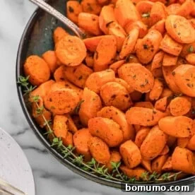 Roasted carrots with thyme and nutmeg in a dark colored bowl, accompanied by a silver spoon.