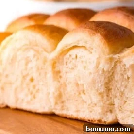A close-up of soft, fluffy Parker House rolls arranged on a wooden board, ready to be enjoyed.
