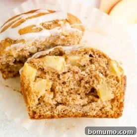 A glazed apple cider muffin, cut in half to reveal tender chunks of apple within its fluffy texture.