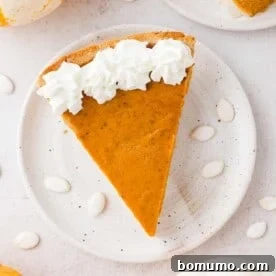 A perfect slice of homemade pumpkin pie, viewed from above, generously topped with a dollop of whipped cream.