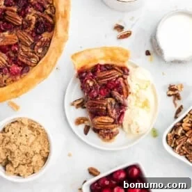 An overhead view of a festive cranberry pecan pie on a white plate, surrounded by ingredients, suggesting abundance.