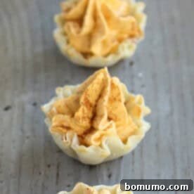 A row of charming mini pumpkin pie tarts on a rustic wooden table, perfect for individual servings.