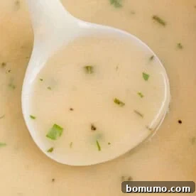 Rich, homemade make-ahead turkey gravy being served in a white ladle.