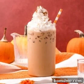 A decadent iced pumpkin spice latte, generously topped with whipped cream, set against a warm orange background.