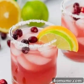 A stunning cranberry margarita in a salt-rimmed glass, garnished with a lime wedge, orange wedge, and fresh cranberries.