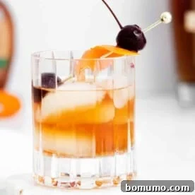 A maple old fashioned cocktail, served on ice with an orange peel and a couple of cherries.