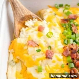 A hearty scoop of loaded mashed potato casserole, rich with cheese and bacon, being served with a wooden spoon.