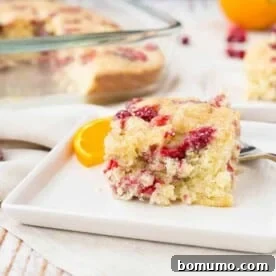 A single serving of moist cranberry coffee cake on a square white plate, with the baking pan visible in the background.