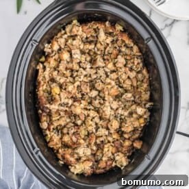 An overhead view of savory crockpot stuffing cooking in a black slow cooker, staying moist and flavorful.