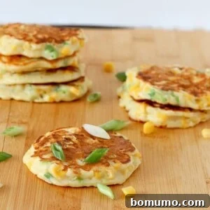Several savory corn cakes on a wooden cutting board, garnished with sliced green onions and corn kernels, a perfect representation of the finished dish.