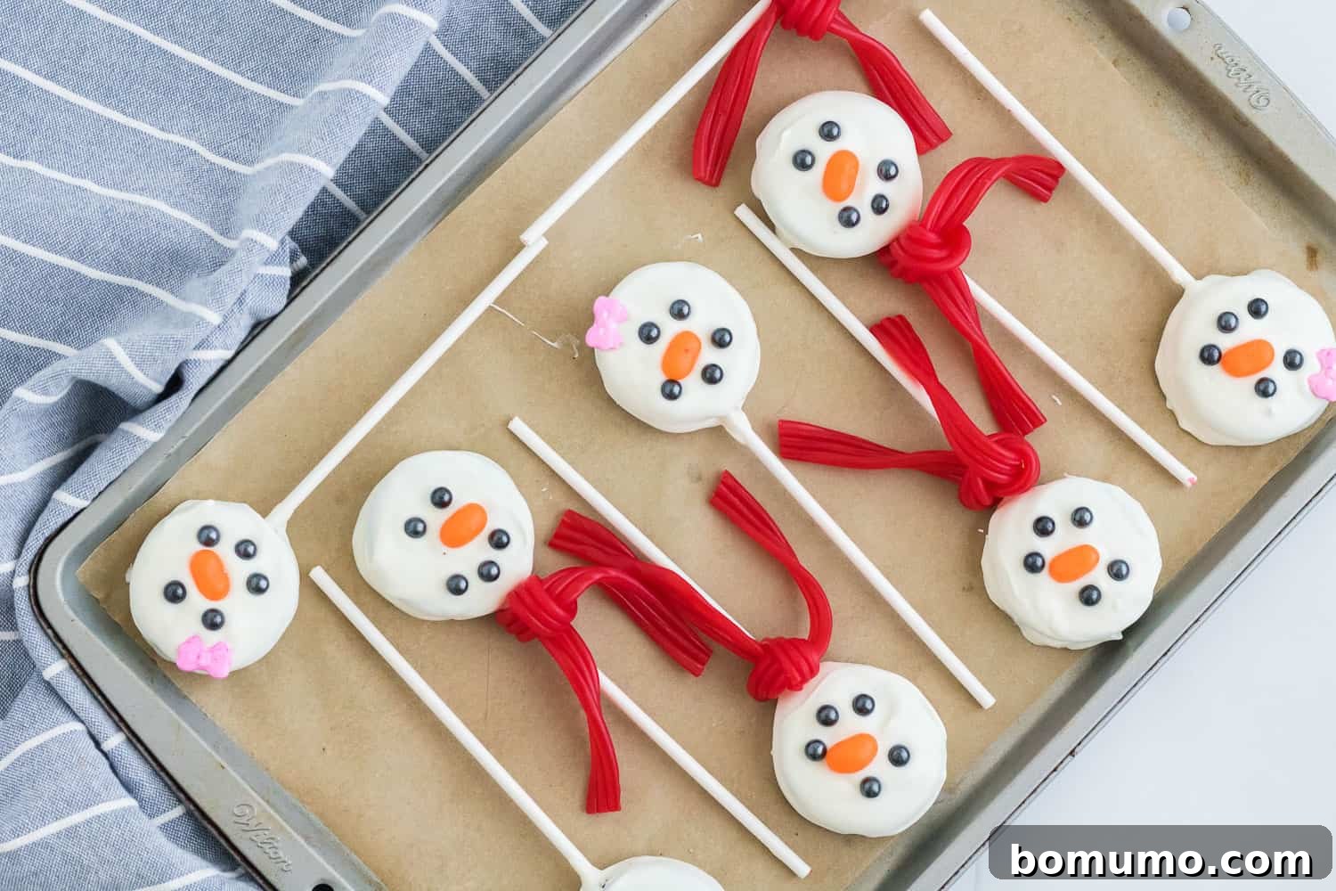 Oreo snowmen pops with scarves on a parchment lined baking sheet.