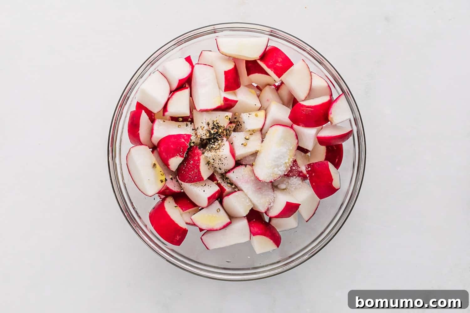 Radishes cut in half and mixed with salt and pepper, ready for roasting.