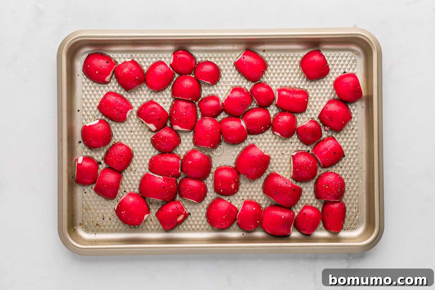 Radishes arranged with their cut side down on a sheet pan, ready for the oven.