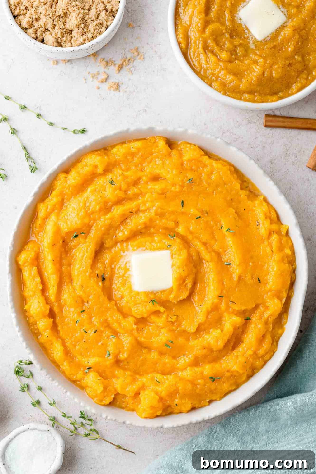 Savory mashed butternut squash in a large bowl, topped with butter. Sweet version also partially visible.
