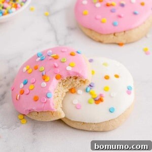 Two frosted cookies, pink and white, pink with a bite taken out.