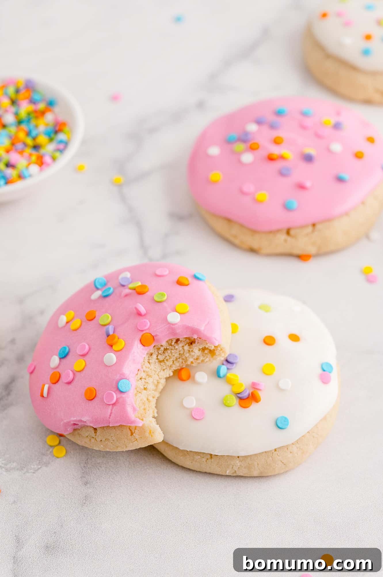 Pink cookie with bite out of it, on top of white frosted cookie.
