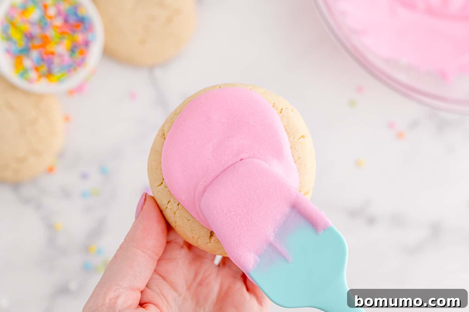 Cookie being frosted with pink icing.