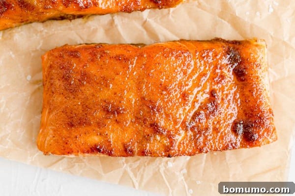 Oven-baked BBQ salmon fillet, tender and ready for glazing. A perfectly baked BBQ salmon fillet resting on a piece of parchment paper, ready for its final glaze.