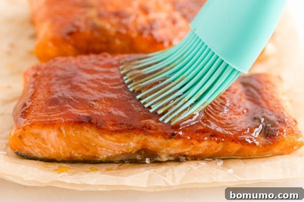 The final touch: brushing sweet and smoky barbecue sauce onto the salmon. A pastry brush expertly applying a rich, glossy barbecue sauce glaze onto a cooked salmon fillet.