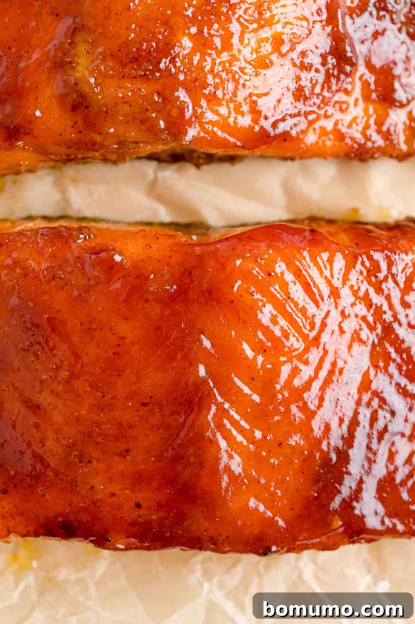 Exquisite BBQ salmon fillets, perfectly glazed and ready to be served. A close-up view of two succulent BBQ salmon fillets, beautifully glazed with barbecue sauce, resting on parchment paper with a perfect sheen.