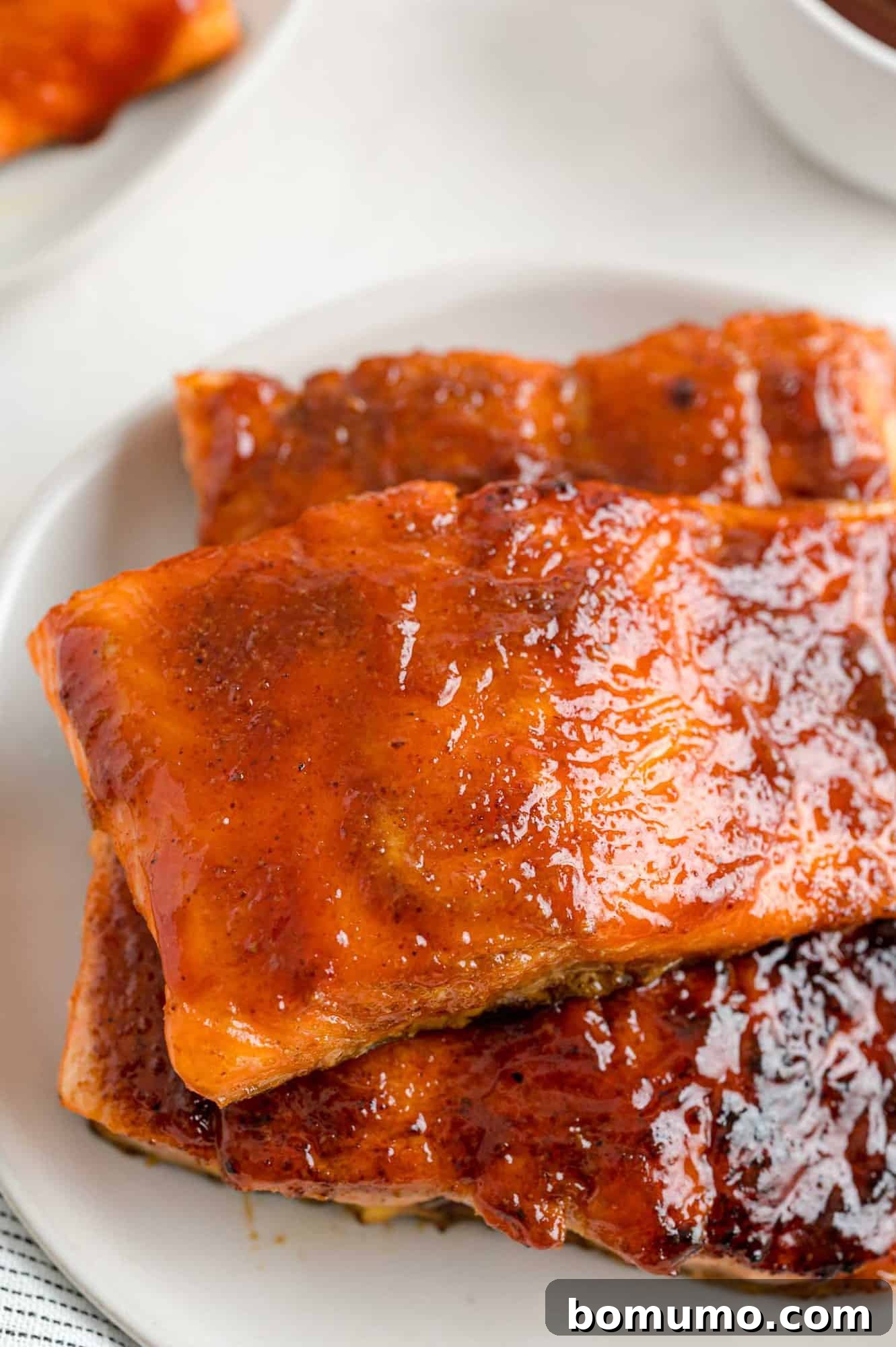 Stacked BBQ salmon fillets, a testament to a delicious and easy dinner. Two generous portions of BBQ salmon fillets, stacked neatly on a white plate, showcasing their rich color and inviting texture.