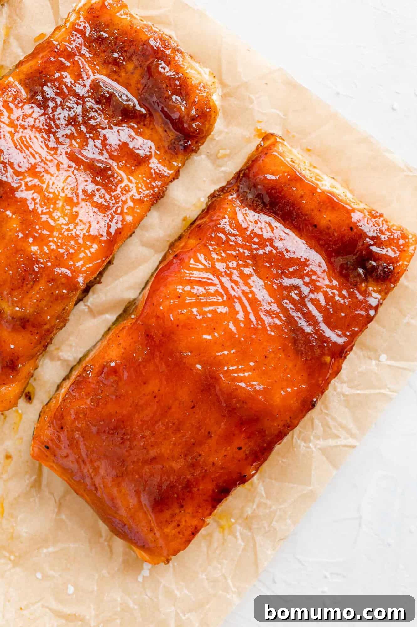 Perfectly glazed BBQ salmon, a tempting sight. A close-up of a beautifully glazed BBQ salmon fillet on parchment paper, highlighting its sticky, sweet, and smoky coating.