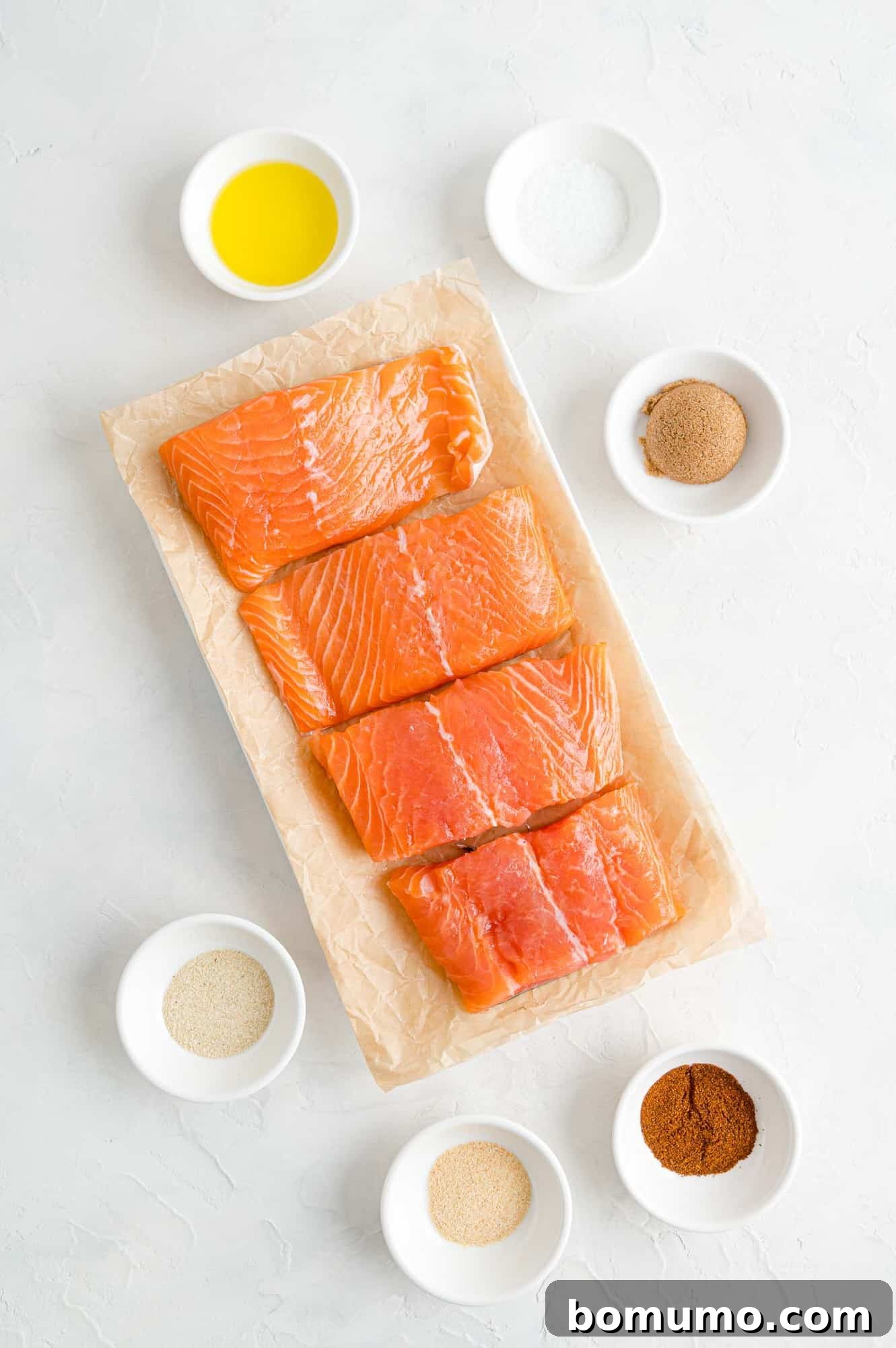 All the fresh ingredients you need to create a mouthwatering BBQ salmon dinner, featuring a homemade spice rub. A vibrant selection of ingredients for BBQ salmon, including fresh salmon fillets, various spices in small bowls, and olive oil, laid out on a clean surface.