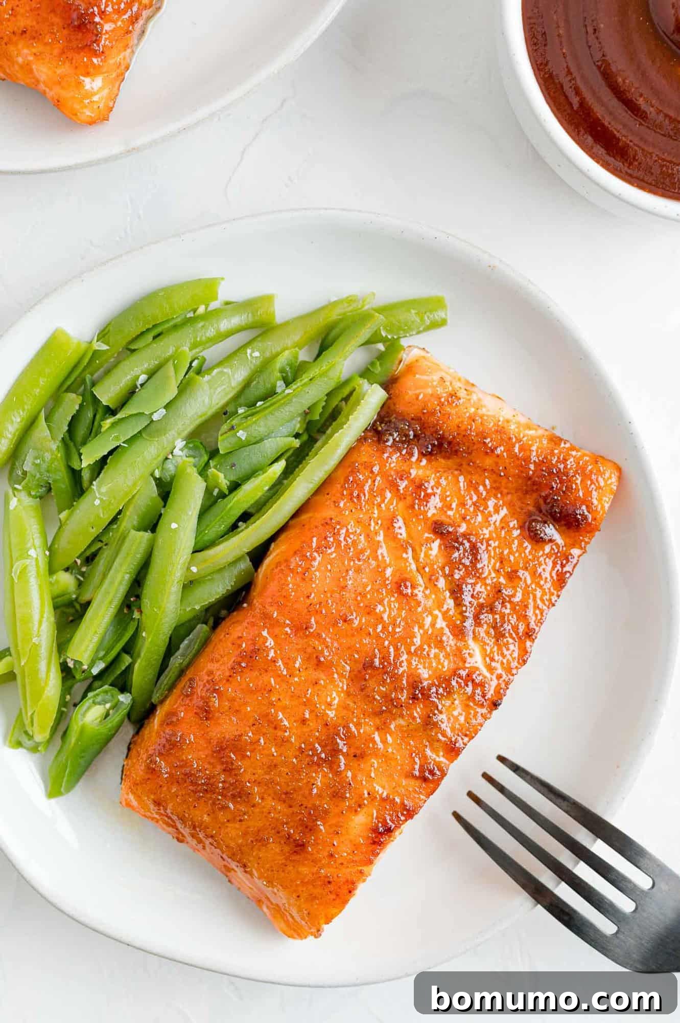 Enjoy this delightful BBQ salmon, a perfect and healthy meal served with fresh green beans. A beautifully cooked BBQ salmon fillet, perfectly flaked with a fork, resting on a white plate alongside fresh steamed green beans.