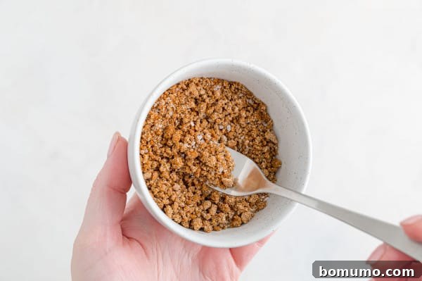 Mixing the aromatic dry rub for the perfect BBQ salmon flavor. A hand mixing the salmon seasoning ingredients in a small white bowl with a fork, creating a rich brown dry rub.